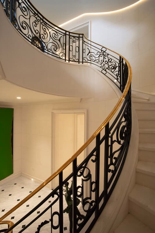 Curved limestone staircase with bronze handrail and cove lighting