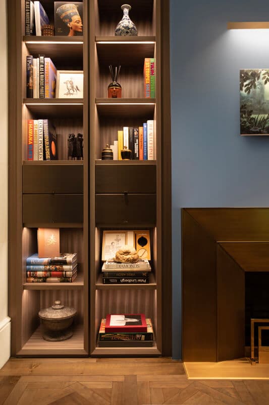 Millwork shelving with integrated lighting beside a bronze fireplace