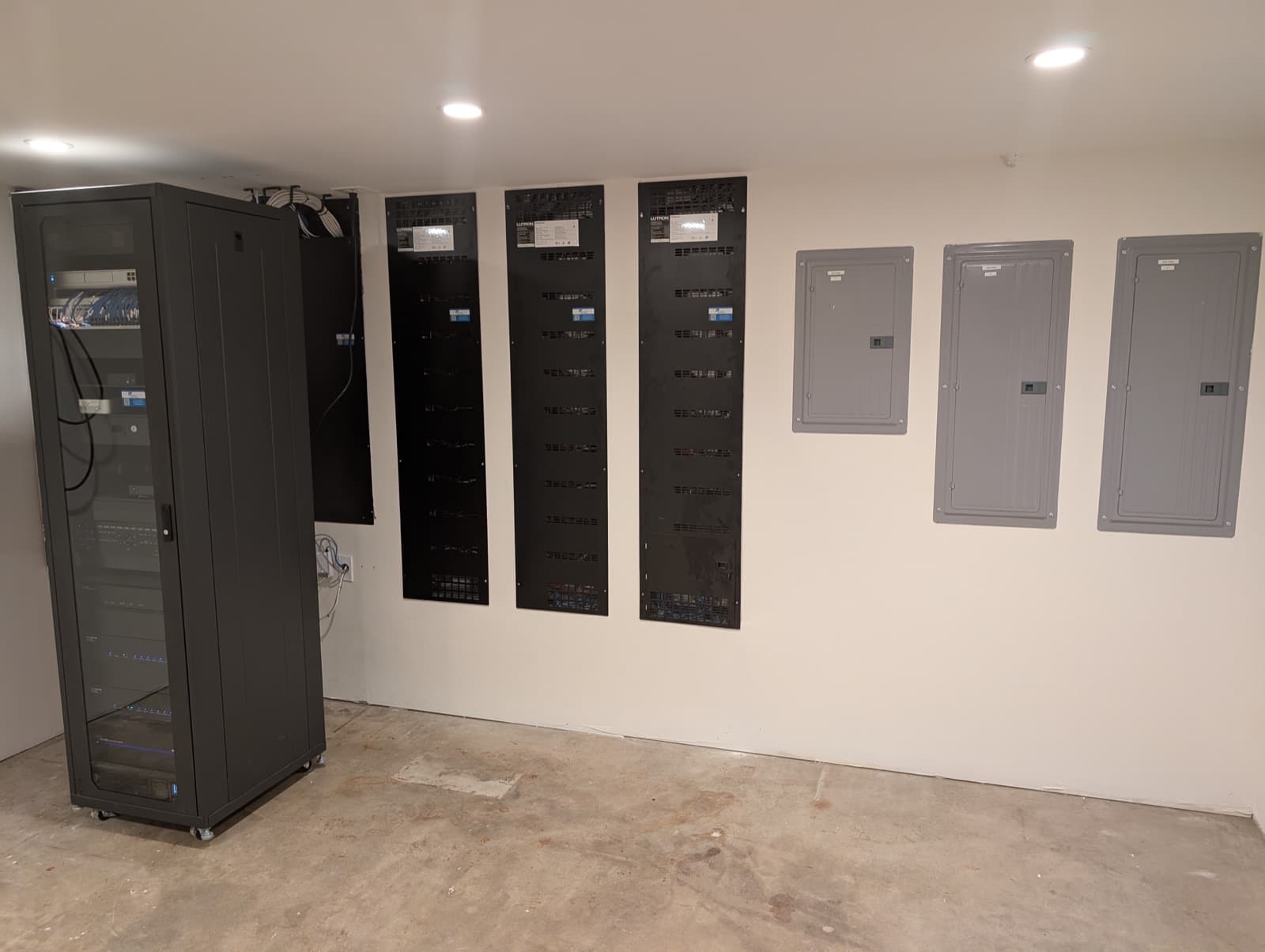 A finished equipment room with a glass-door rack and a row of Lutron lighting panels on a white wall