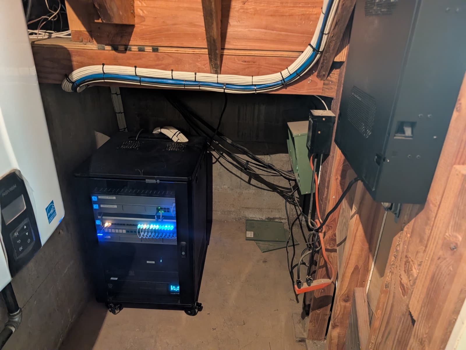 A closed black network rack in a basement with cable bundles dressed neatly along the joists